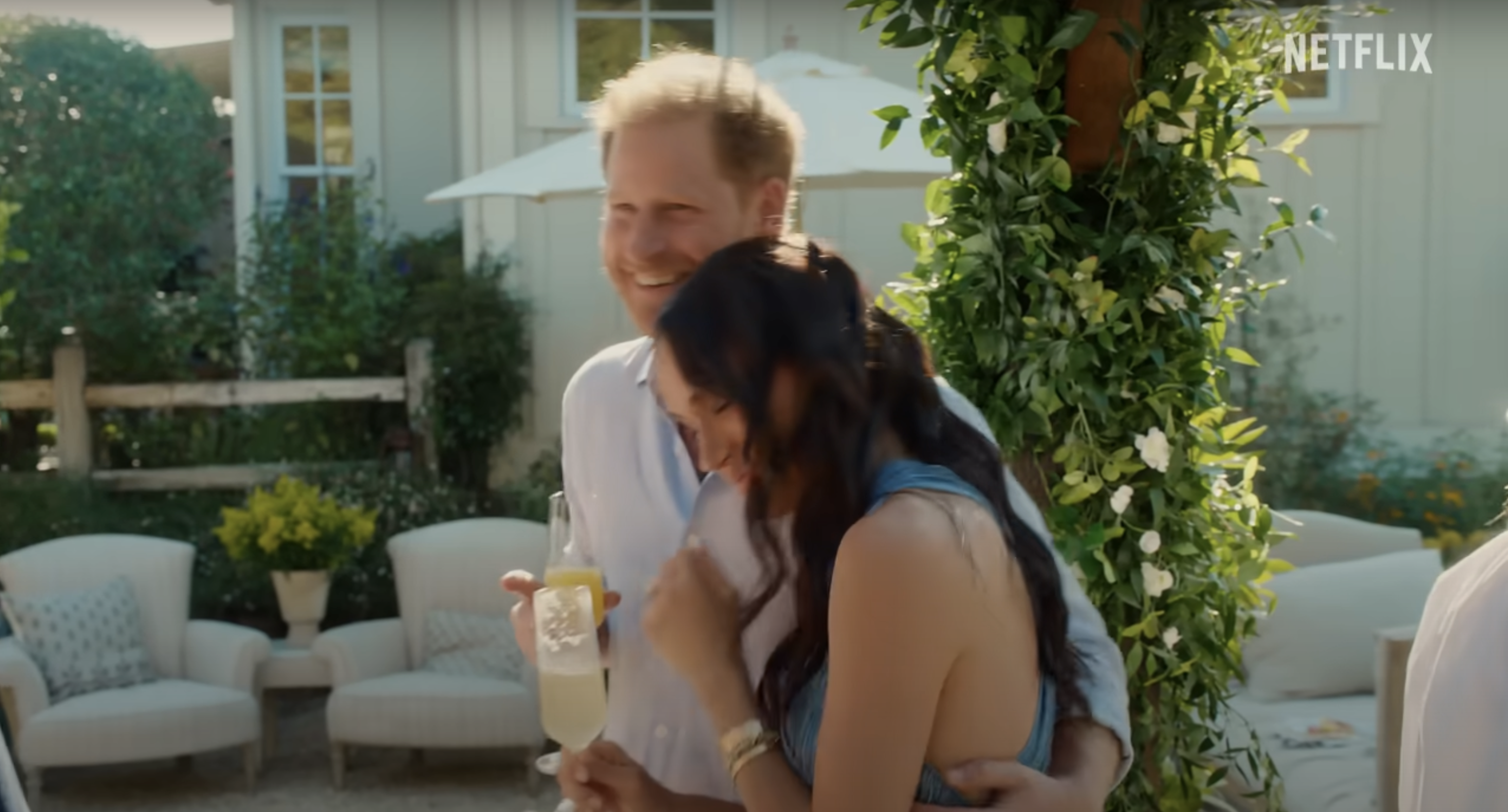 Harry and Meghan laughing and hugging outside in a garden