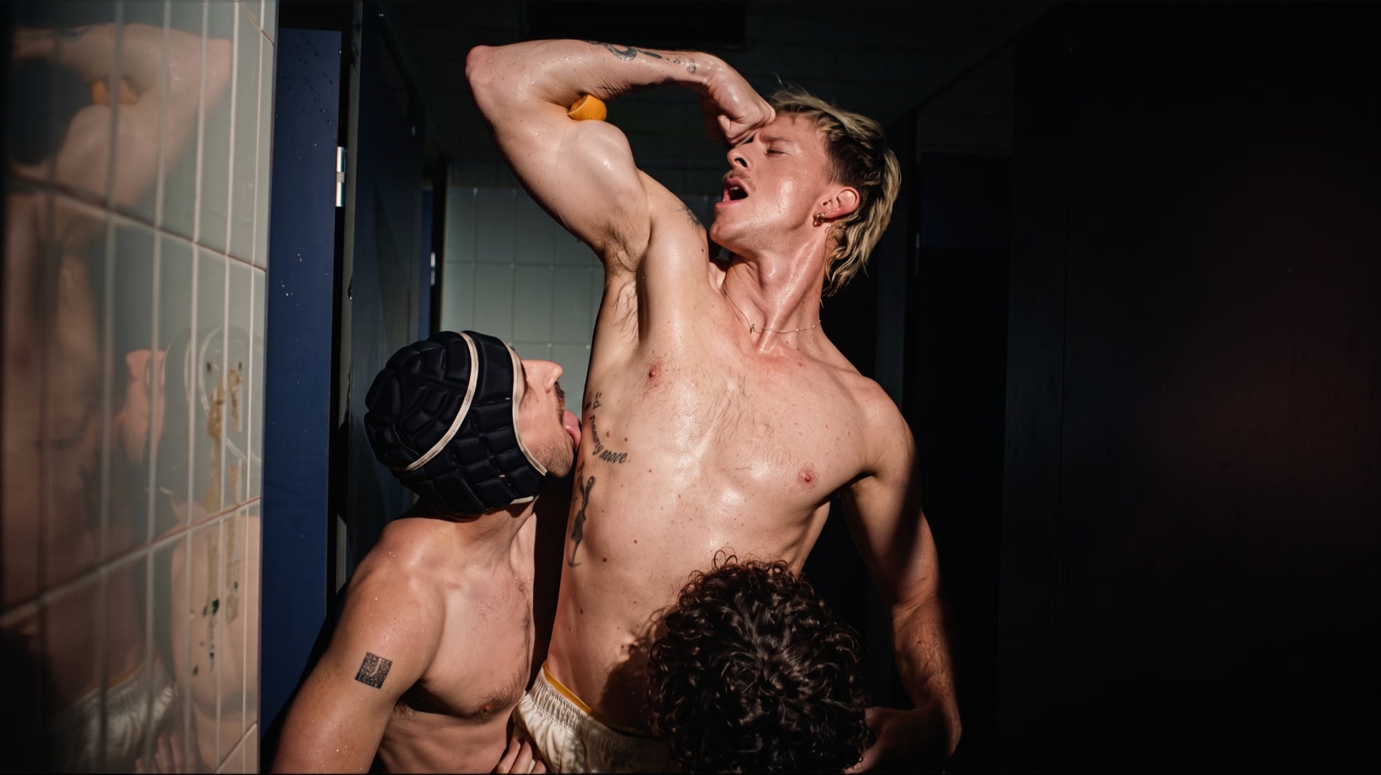 A man raising his arm beside two other men in a tiled shower room.