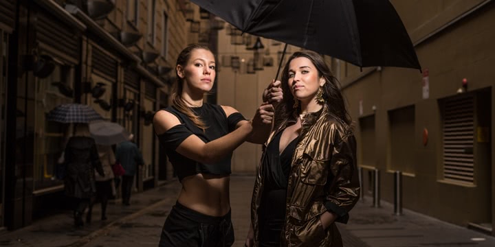 Two members of hip hop group Coda Conduct, Sally Coleman and Erica Mallett, hold a black umbrella in a laneway