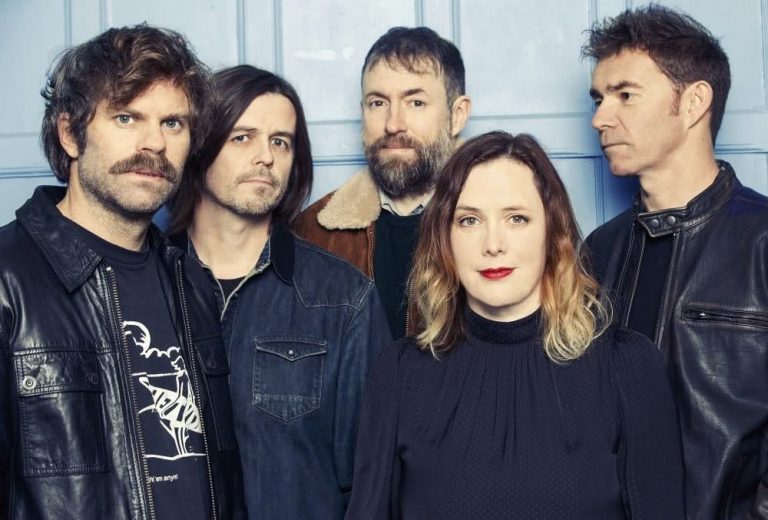 The members of Slowdive standing in front of a blue wall