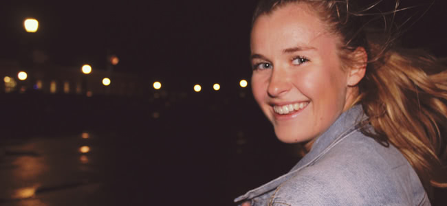 Girl with blond hair looking back at camera wearing a denim jacket at night time