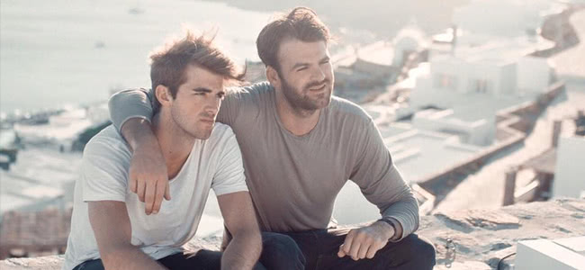The Chainsmokers band members sitting on a ledge wearing a grey and white top