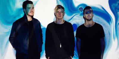 Rufus band members wearing black standing in front of a blue and white wall