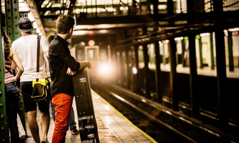 A man with a guitar case waits for a train in the New York Subway