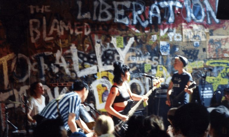 Bikini Kill play live against a wall of graffiti