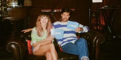 Josephine and Anthony sit on couch about to play 'Who's Most Likely To?' Game