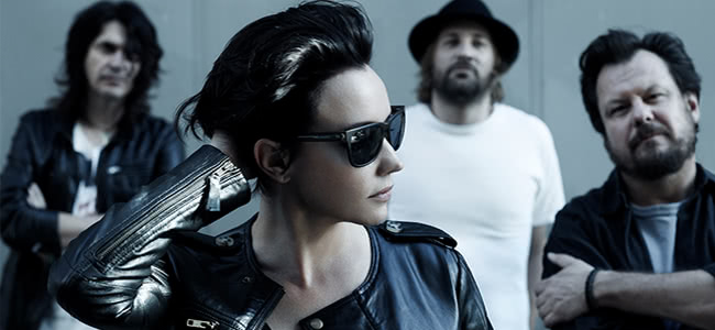 three men standing in the background and a woman standing closer to the camera all wearing black and white clothing woman wearing sunglasses looking away from the camera